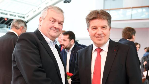 Zwei Männer in Anzügen stehen lächelnd nebeneinander.