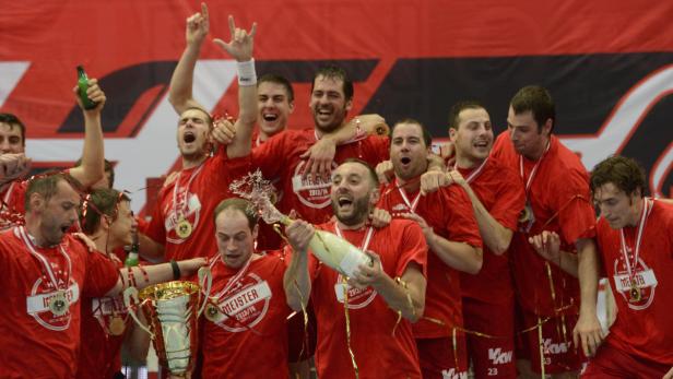 Eine Gruppe Handballspieler feiert einen Sieg mit Champagner und einem Pokal.