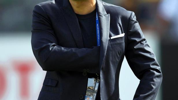 Luís Figo mit Sonnenbrille, Sakko und Jeans auf einem Rasenplatz.