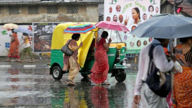 Im Regen gehen Menschen mit Schirmen an einem Autorikscha vorbei.