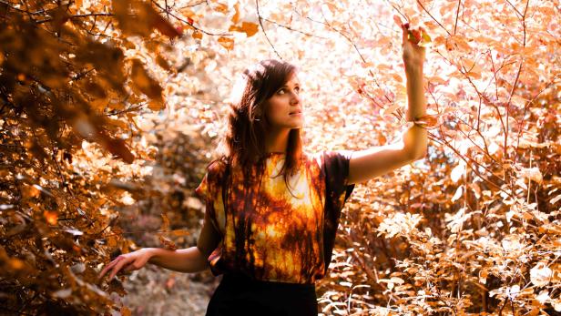 Eine Frau steht im Herbstwald und berührt einen Ast.