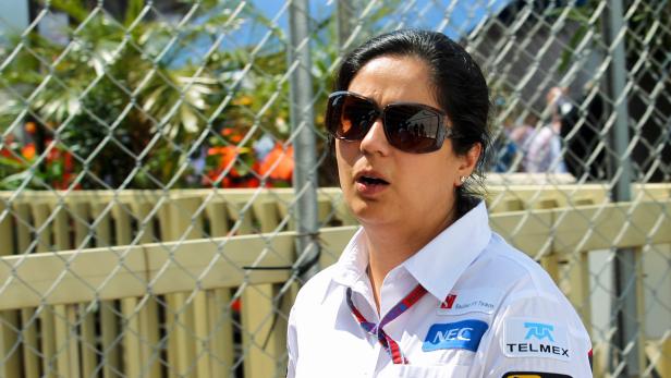 Eine Frau mit Sonnenbrille und Hemd des Sauber F1 Teams steht vor einem Zaun.