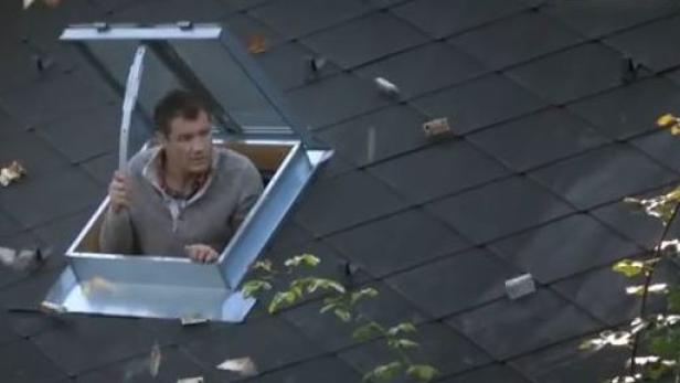 Ein Mann schaut aus einem Dachfenster auf einem schiefergedeckten Dach.