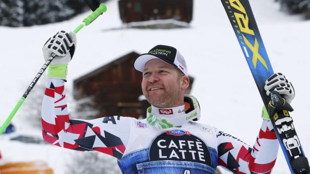 Ein lächelnder Skirennläufer mit Skiern und Stöcken in der Hand feiert.