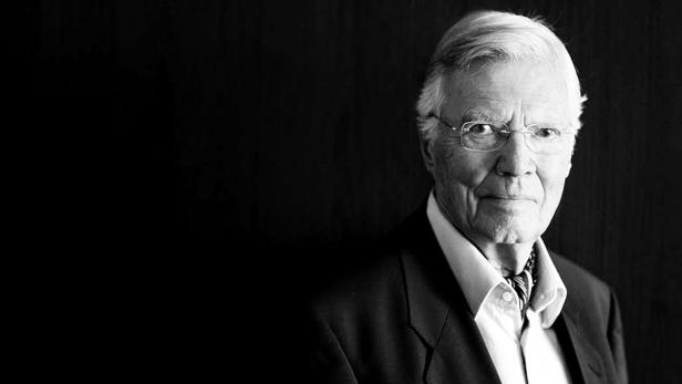 Ein älterer Mann mit Brille und Anzug in Schwarzweiß.