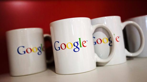 Mehrere weiße Tassen mit dem Google-Logo stehen auf einem Regal.