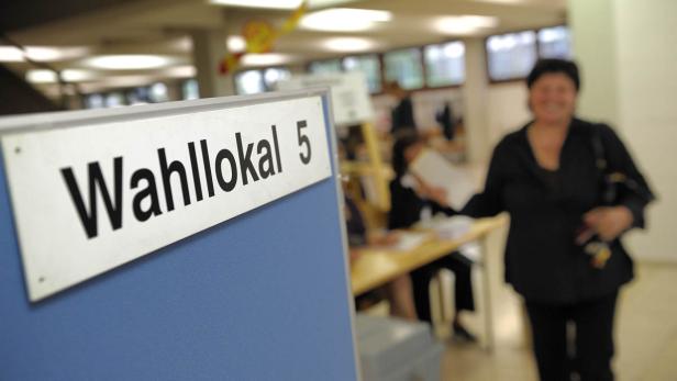 Ein Schild mit der Aufschrift „Wahllokal 5“ in einem Wahllokal mit einer Wählerin im Hintergrund.