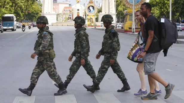 Drei Soldaten und ein Paar überqueren eine Straße in Bangkok.
