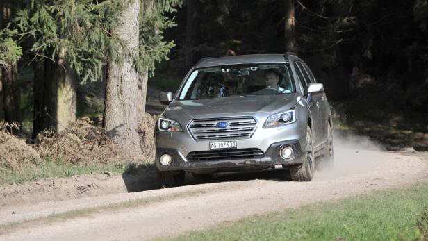 Ein grauer Subaru fährt auf einer unbefestigten Straße durch einen Wald.