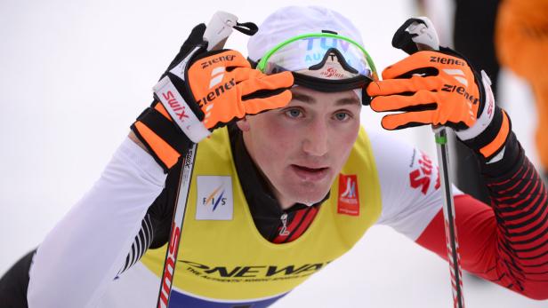 Ein Langläufer mit Skibrille und orangefarbenen Handschuhen vor einem Rennen.