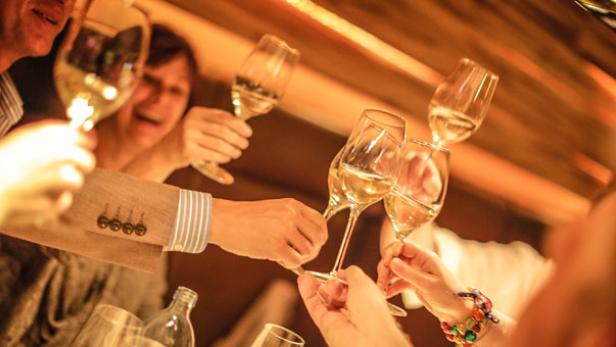 Eine Gruppe von Menschen stößt mit Weißweingläsern an.