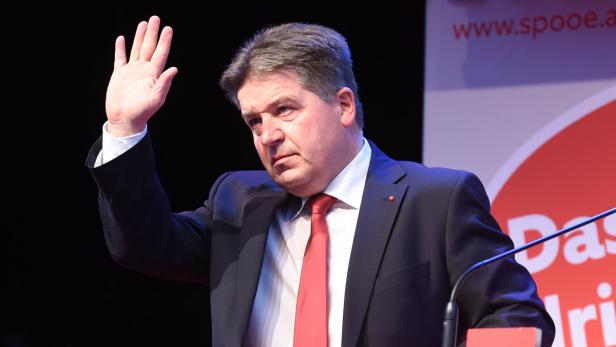 Ein Mann im Anzug hebt seine Hand vor einem SPÖ-Hintergrund.