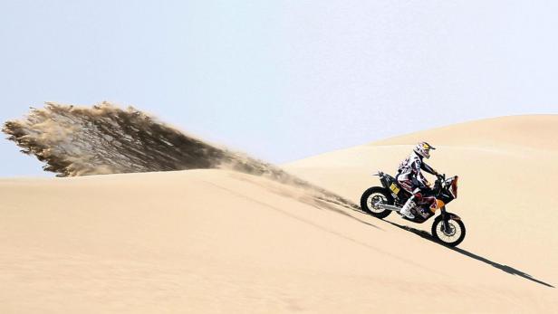 Ein Motorradfahrer fährt eine Sanddüne hinunter und wirbelt Sand auf.