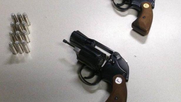 Zwei Revolver und eine Reihe von Patronen liegen auf einem Tisch.