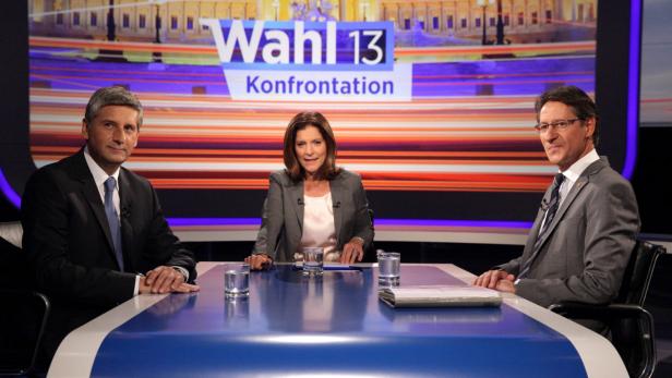 Drei Personen sitzen an einem Tisch vor dem Hintergrund der „Wahl 13“-Konfrontation.