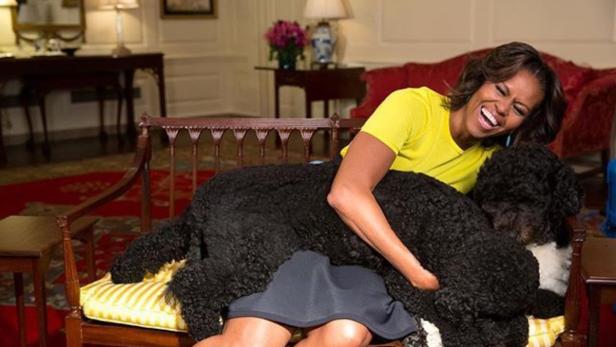 Michelle Obama umarmt lachend ihren Hund Bo auf einer Bank.