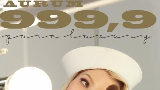 Eine Frau mit weißer Kopfbedeckung vor einem Spiegel mit der Aufschrift „Aurum 999,9 pure luxury“.