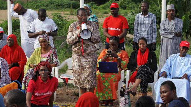 Eine Frau spricht durch ein Megaphon bei einer Kundgebung; einige tragen „#BringBackOurGirls“-Shirts.