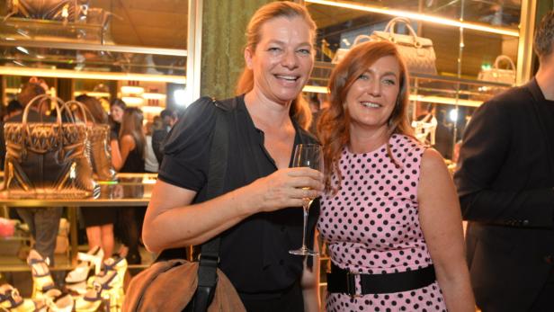 Zwei Frauen posieren lächelnd mit einem Glas Sekt in einem Geschäft.