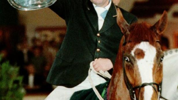 Ein Reiter hält eine silberne Trophäe auf dem Rücken eines Pferdes.