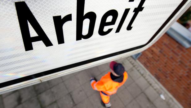 Ein Bauarbeiter geht unter einem Schild mit der Aufschrift „Arbeit“.
