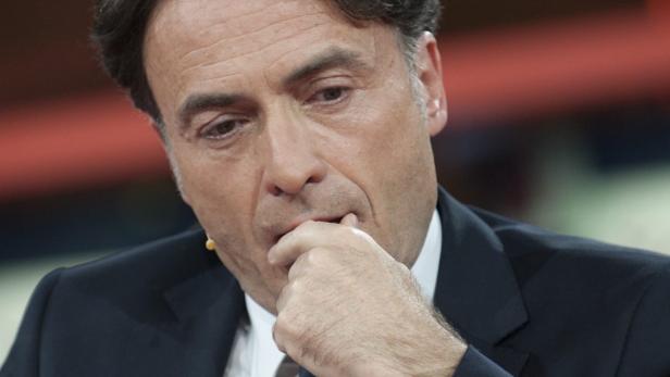 Ein Mann in einem dunklen Anzug kaut nachdenklich auf seinen Fingern.