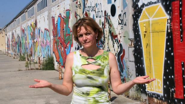 Eine Frau steht vor einer Wand mit Graffiti und breitet ihre Arme aus.