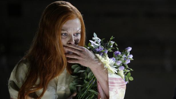 Eine Frau mit roten Haaren weint und hält einen Blumenstrauß in den Händen.