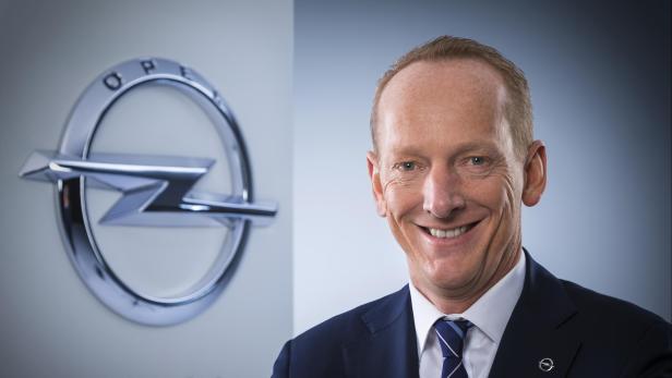 Ein lächelnder Mann im Anzug vor dem Opel-Logo.