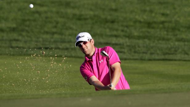 Ein Golfspieler im pinkfarbenen Hemd schlägt einen Ball aus einem Sandbunker.