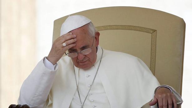 Papst Franziskus sitzt mit gesenktem Kopf und hält eine Hand an die Stirn.