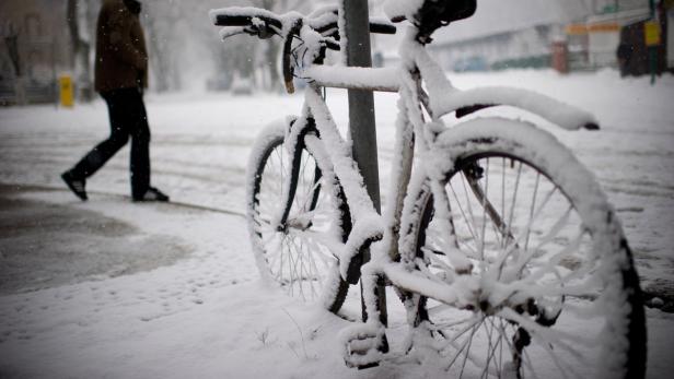 Ein mit Schnee bedecktes Fahrrad lehnt an einem Laternenpfahl.