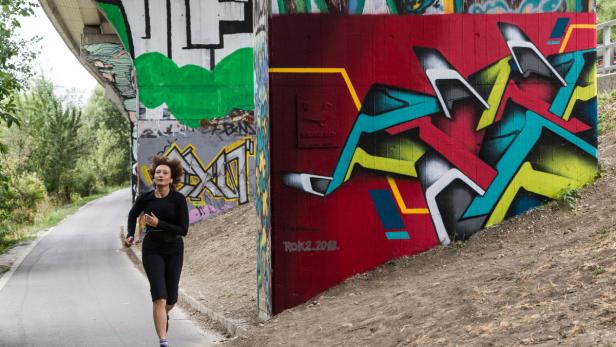Eine Frau joggt auf einem Weg unter einer Brücke mit Graffiti.