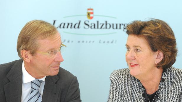 Zwei Personen sitzen vor einem Hintergrund mit dem Logo des Landes Salzburg.