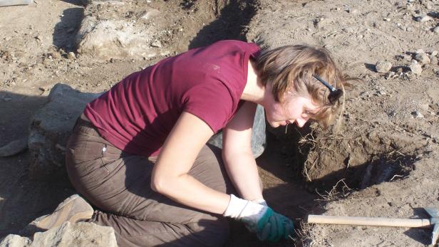Eine Frau kniet und gräbt mit Handschuhen in einem Loch.