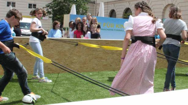 Kinder spielen mit Gummibändern an einem Stand mit der Aufschrift „Erwachsene Fussball“.