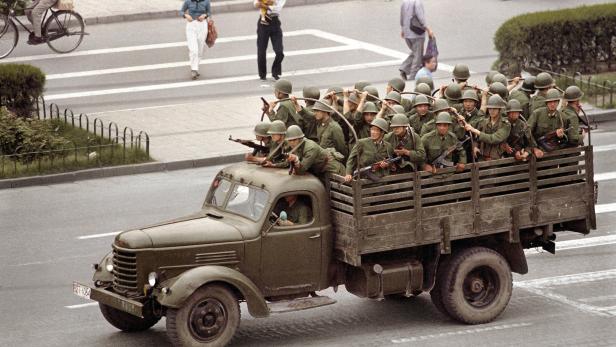 Soldaten mit Gewehren fahren auf einem Lastwagen durch eine Stadt.
