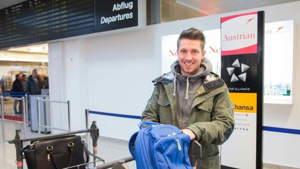 Ein lächelnder Mann mit Rucksack steht im Abflugbereich eines Flughafens.