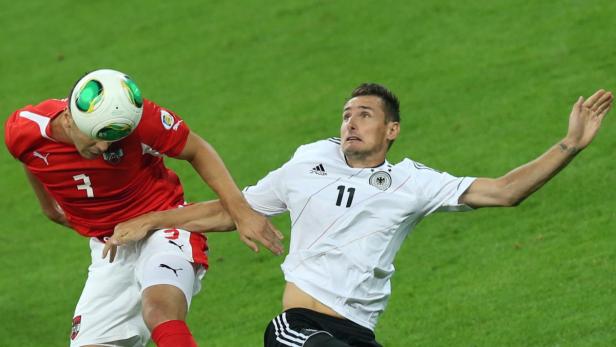 Ein österreichischer Spieler köpft den Ball, während ein deutscher Spieler zusieht.