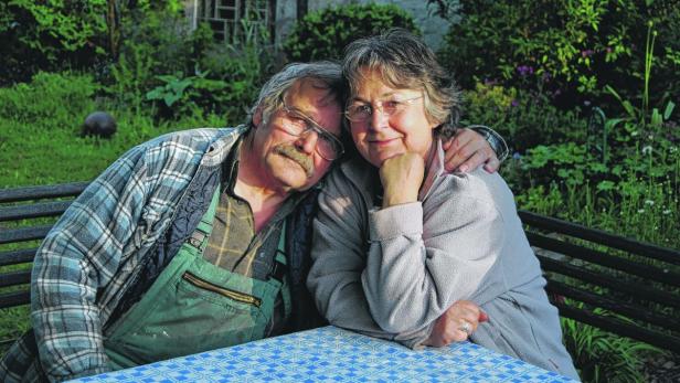 Ein älteres Paar sitzt an einem Tisch im Garten und umarmt sich.