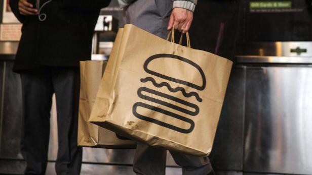 Eine Person trägt eine Papiertüte von Shake Shack.