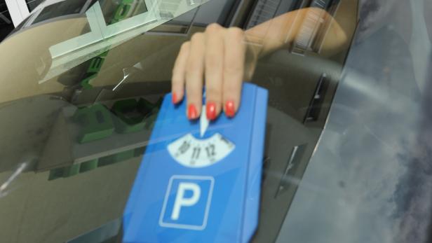 Eine Hand mit rot lackierten Nägeln stellt eine Parkscheibe ins Auto.