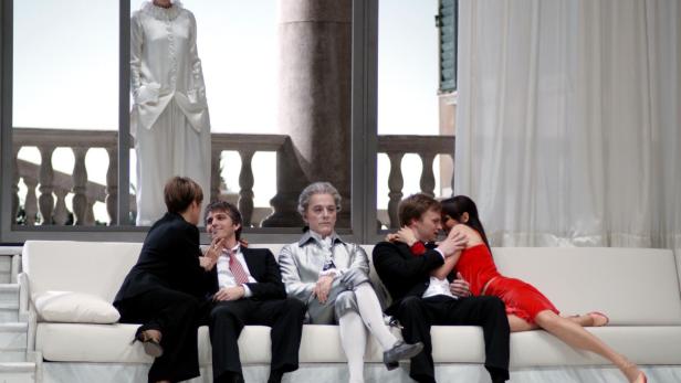 Szene aus einem Theaterstück mit mehreren Darstellern auf einer weißen Couch.