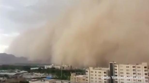 Ein Sandsturm nähert sich einer Stadt vor einer Bergkulisse.