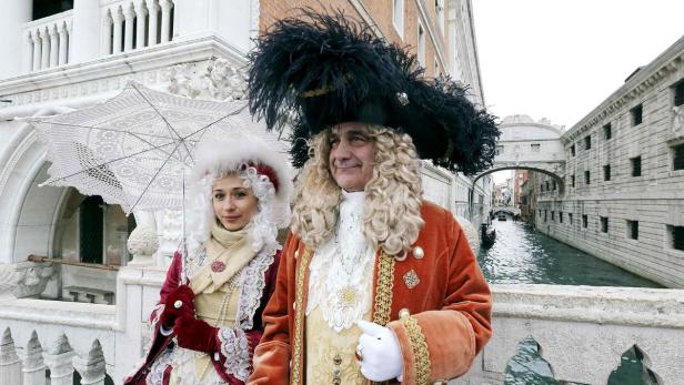 Zwei Personen in venezianischen Kostümen stehen auf einer Brücke in Venedig.