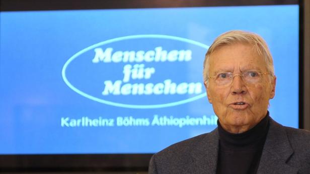 Karlheinz Böhm vor einem Bildschirm mit dem Logo „Menschen für Menschen“.