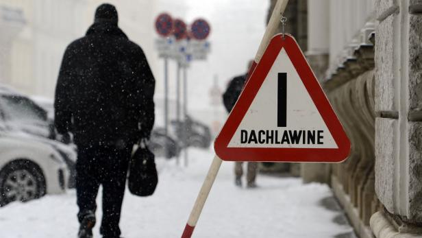 Ein Warnschild „Dachlawine“ steht auf einem verschneiten Bürgersteig.