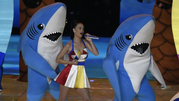 Katy Perry tritt mit zwei Tänzern in Haikostümen auf einer Bühne auf.