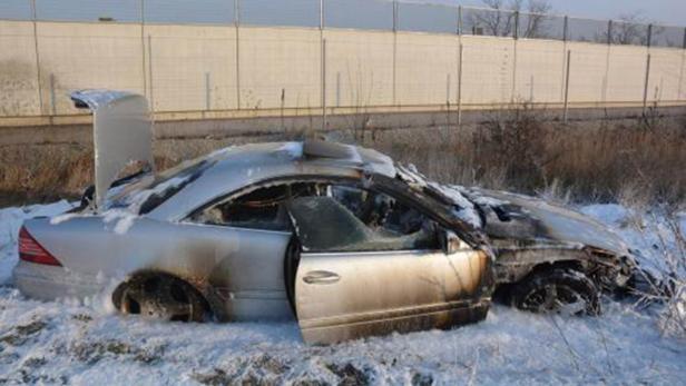 Ein ausgebranntes Auto steht im Schnee neben einer Straße.