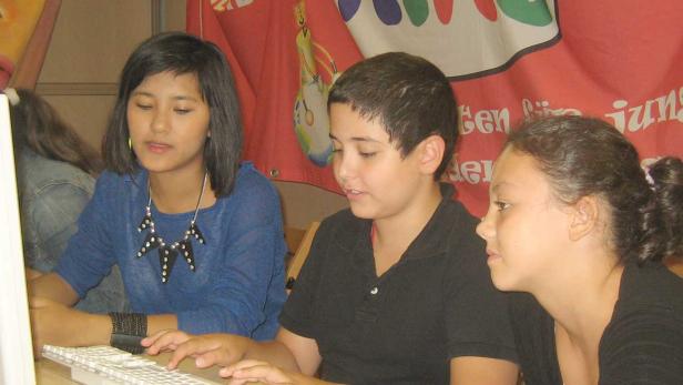 Drei Jugendliche sitzen vor einem Computer und tippen auf der Tastatur.